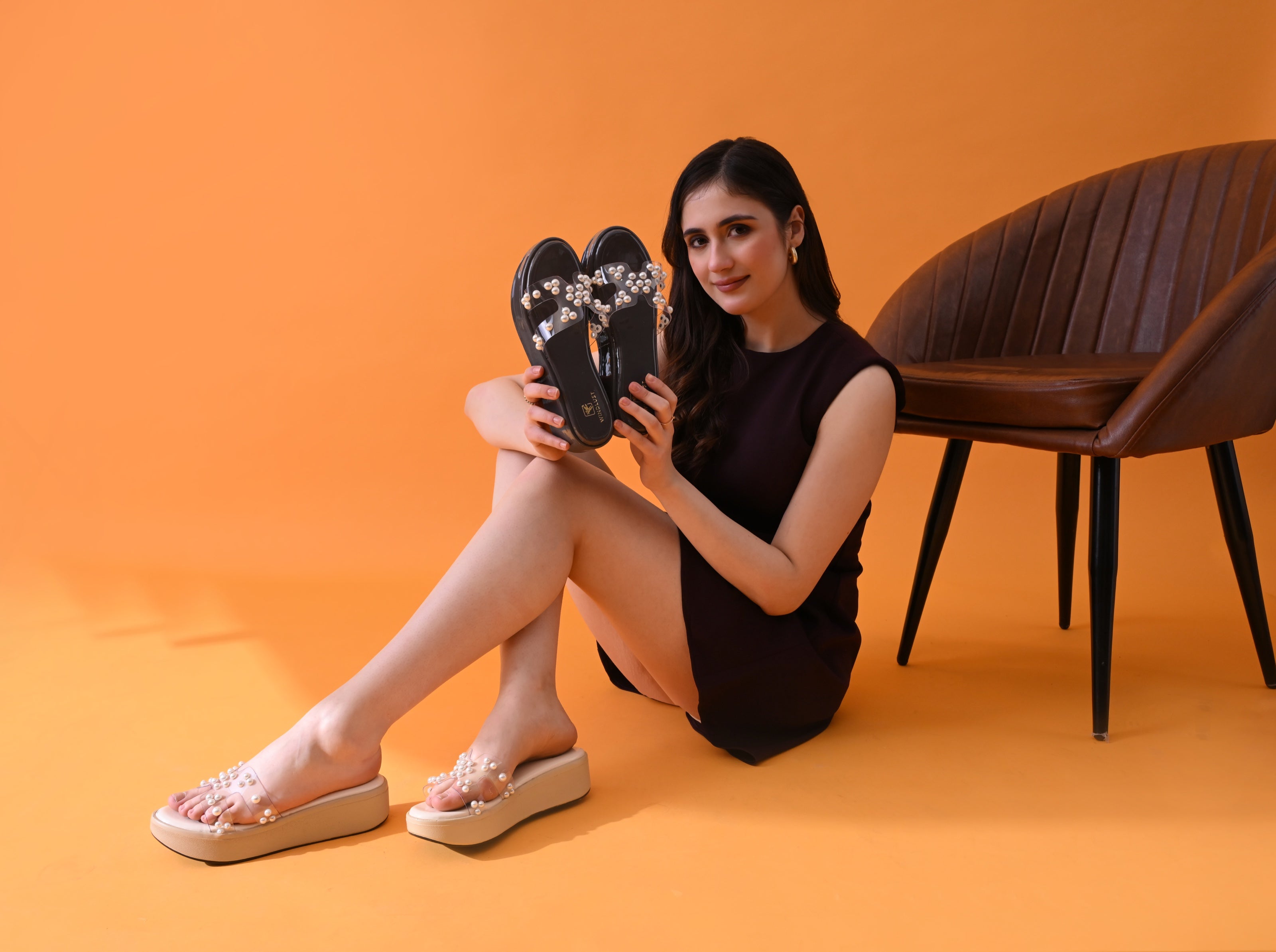Windlust house campaign with model holding branded black platform footwear against the signature orange studio backdrop.