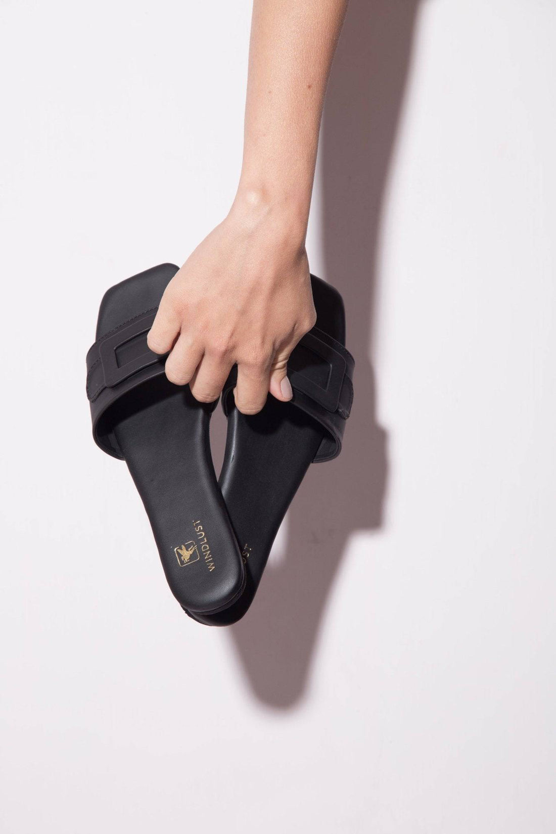 Black Windlust single strap buckled flats with a sleek design, featuring a single strap and buckle detail on the flats.